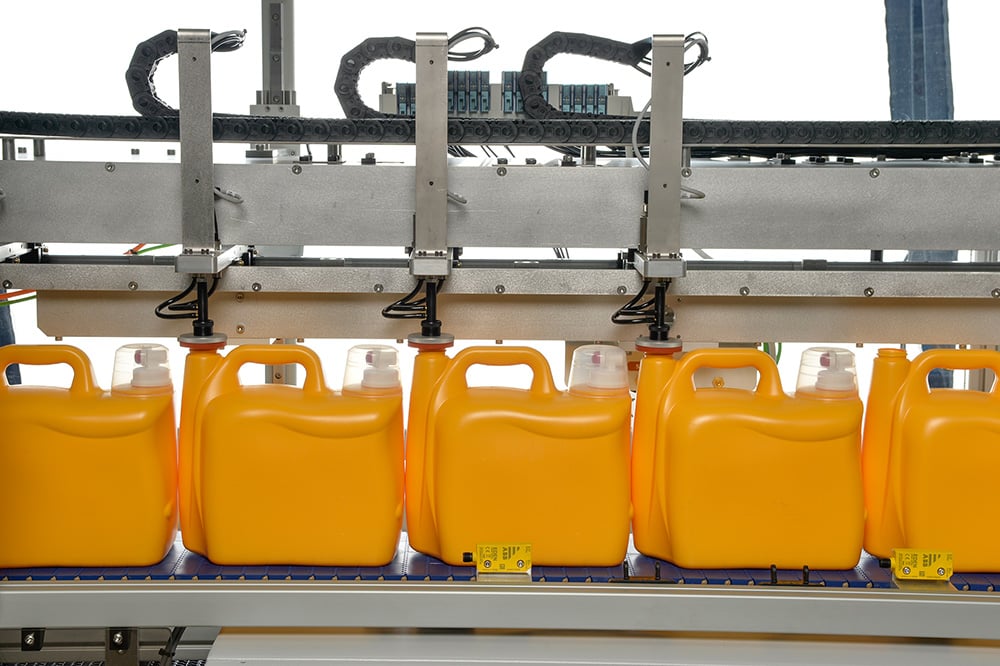 An image of yellow detergent bottles on a conveyor belt being tested for leaks